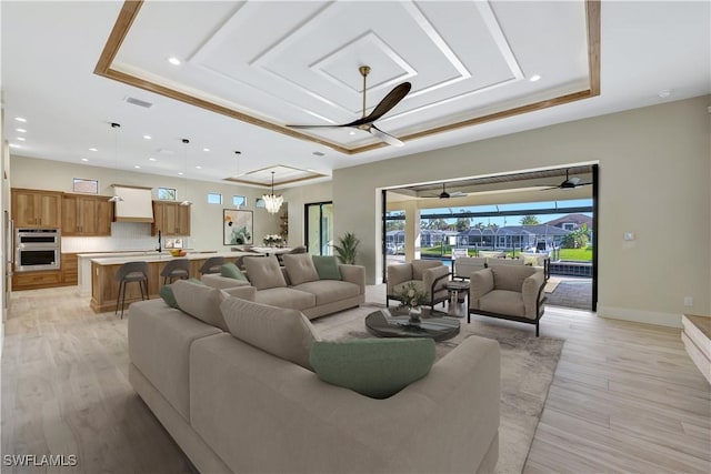 living room featuring ceiling fan, light hardwood / wood-style floors, and a tray ceiling