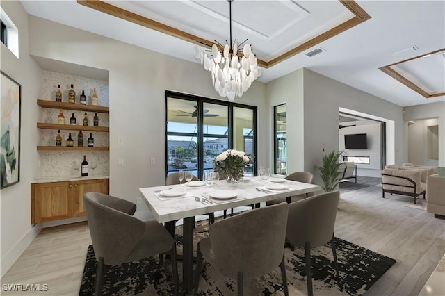 dining space featuring a chandelier, light hardwood / wood-style floors, a raised ceiling, and bar