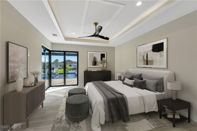 bedroom featuring access to exterior, a tray ceiling, ceiling fan, a water view, and light hardwood / wood-style flooring