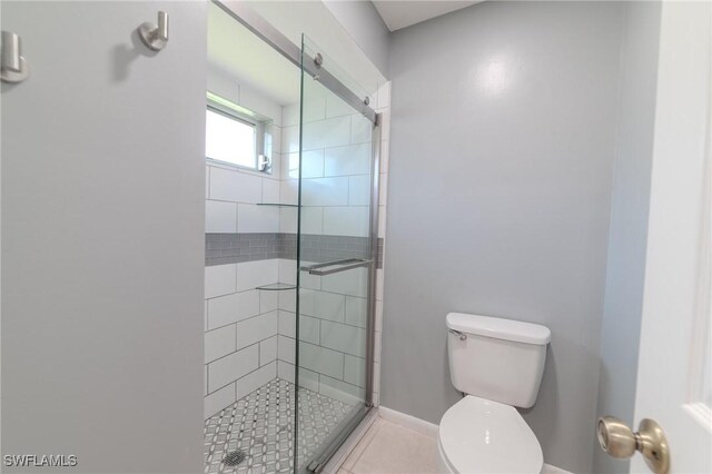 bathroom featuring tile patterned flooring, a shower with shower door, and toilet