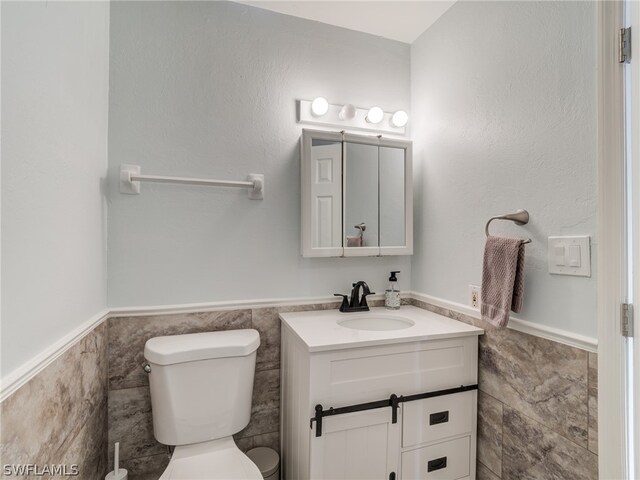 half bath featuring a wainscoted wall, vanity, toilet, and tile walls