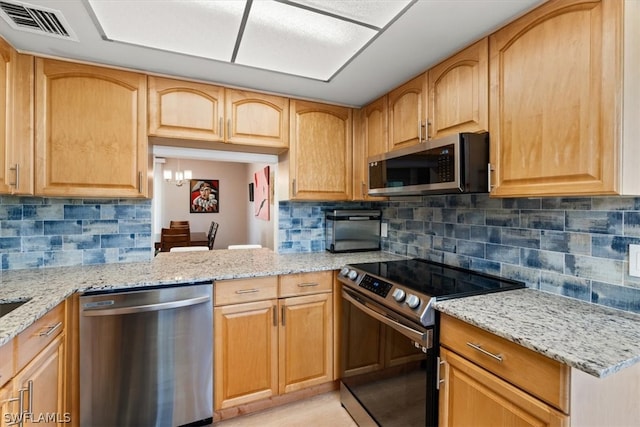 kitchen with appliances with stainless steel finishes, tasteful backsplash, light stone countertops, and a chandelier