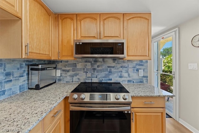 kitchen featuring appliances with stainless steel finishes, light wood-type flooring, backsplash, and light stone counters