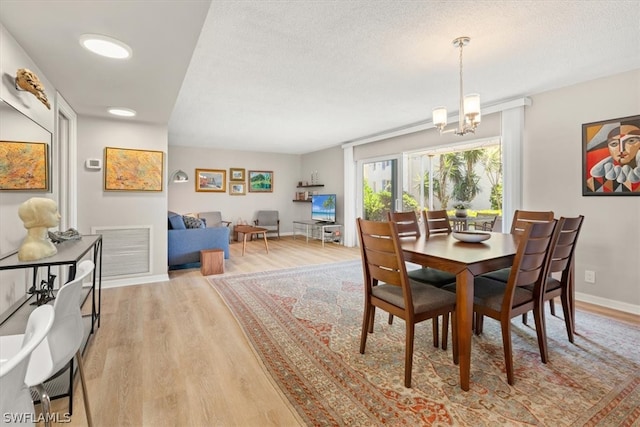 dining space with a chandelier, light wood-type flooring, and a textured ceiling