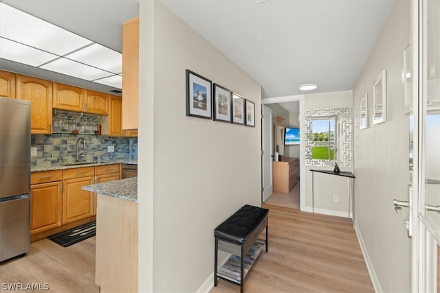 kitchen with light stone countertops, stainless steel refrigerator, light hardwood / wood-style flooring, backsplash, and sink