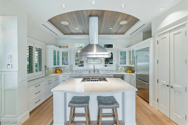 kitchen featuring backsplash, light hardwood / wood-style flooring, a breakfast bar area, a kitchen island, and island range hood