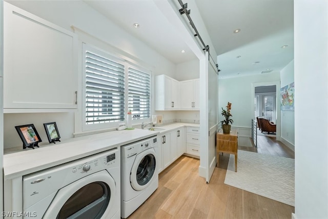 washroom with washer and clothes dryer, cabinets, light hardwood / wood-style floors, and a barn door