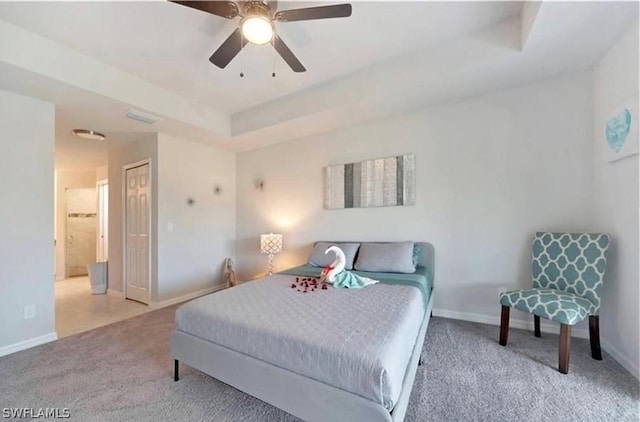 carpeted bedroom featuring a tray ceiling, connected bathroom, ceiling fan, and a closet