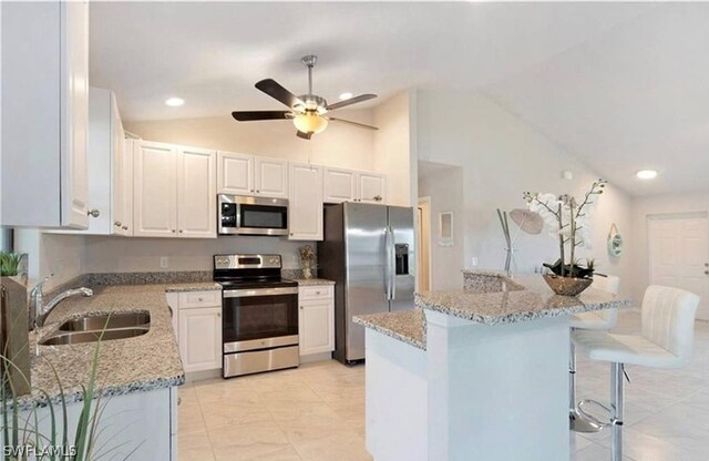 kitchen featuring white cabinetry, sink, vaulted ceiling, a kitchen bar, and appliances with stainless steel finishes