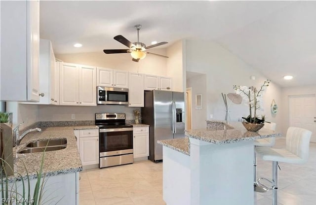 kitchen with a breakfast bar, stainless steel appliances, sink, white cabinets, and lofted ceiling