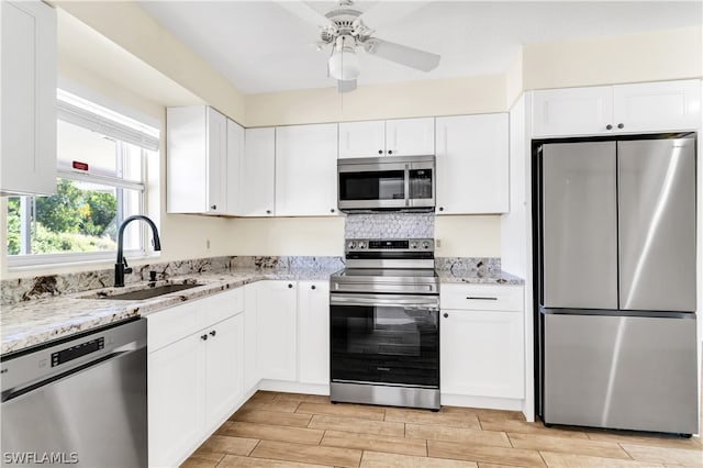 kitchen with white cabinetry, appliances with stainless steel finishes, ceiling fan, light stone counters, and sink