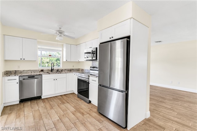 kitchen with light stone countertops, appliances with stainless steel finishes, white cabinets, sink, and light wood-type flooring