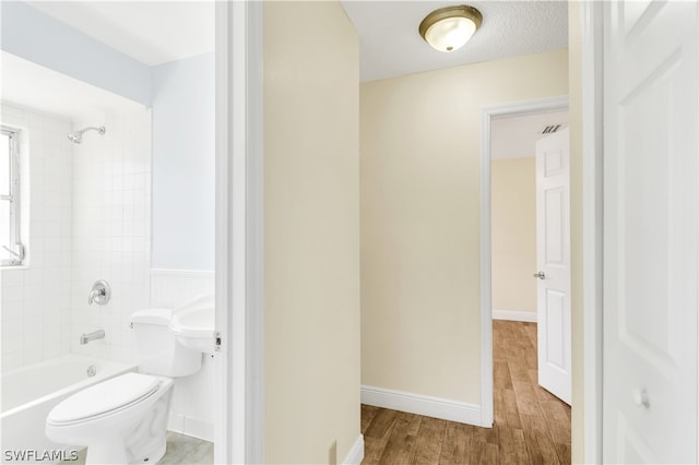 bathroom with a textured ceiling, hardwood / wood-style floors, toilet, and tiled shower / bath