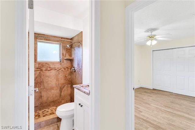 bathroom featuring wood-type flooring, tiled shower, vanity, toilet, and ceiling fan