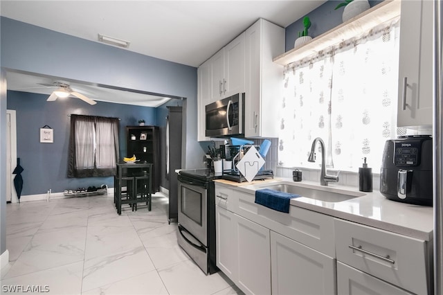 kitchen with stainless steel appliances, light tile patterned floors, ceiling fan, sink, and white cabinetry