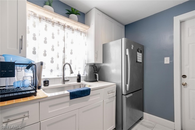 kitchen featuring sink, light tile patterned flooring, white cabinetry, and stainless steel refrigerator