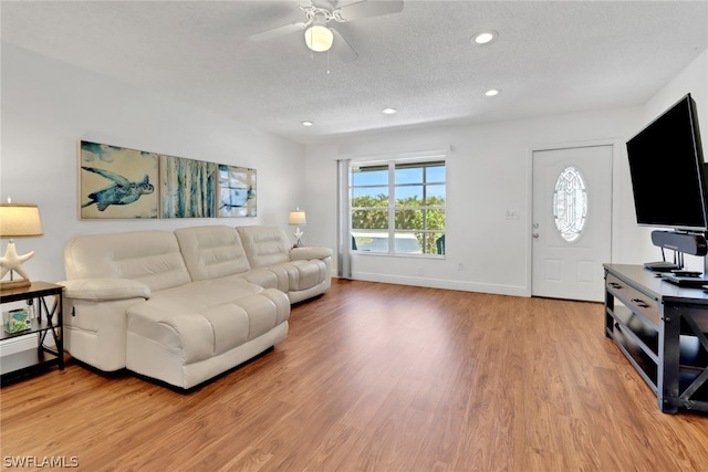 living room featuring light hardwood / wood-style flooring, ceiling fan, and a textured ceiling