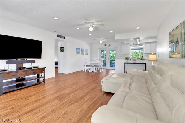 living room with light wood-type flooring, ceiling fan, french doors, and a textured ceiling