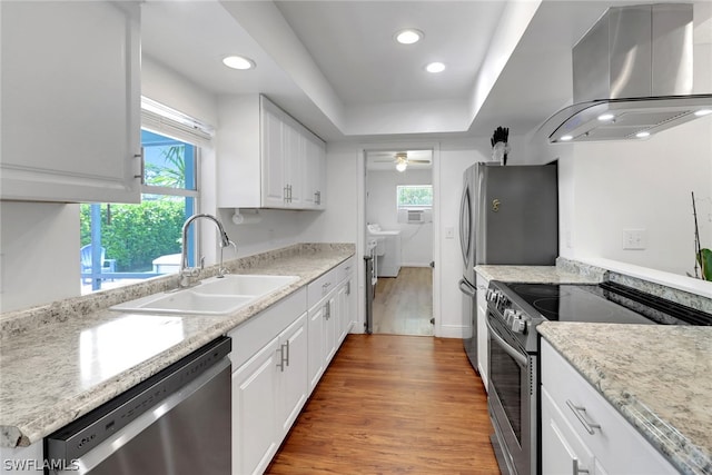 kitchen with white cabinets, sink, exhaust hood, hardwood / wood-style flooring, and stainless steel appliances