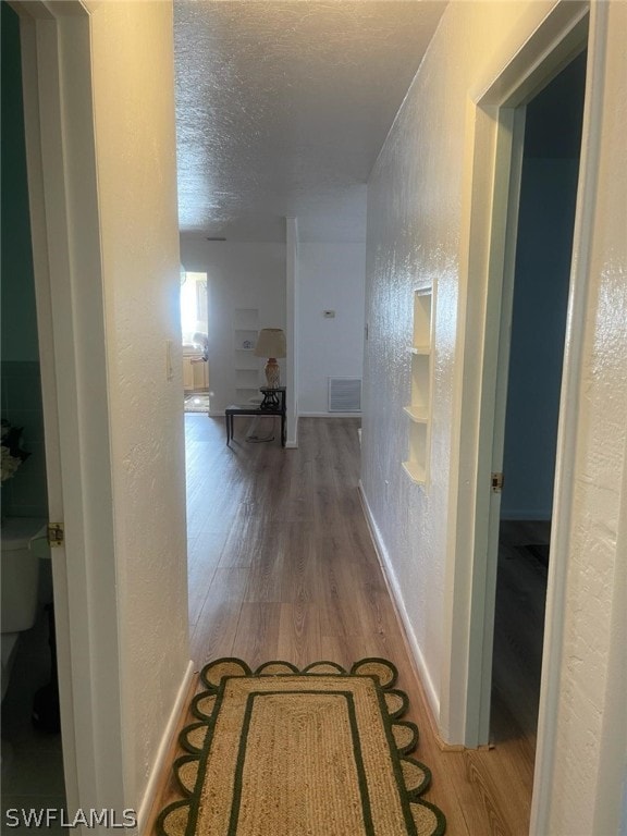 hall with light wood-type flooring and a textured ceiling