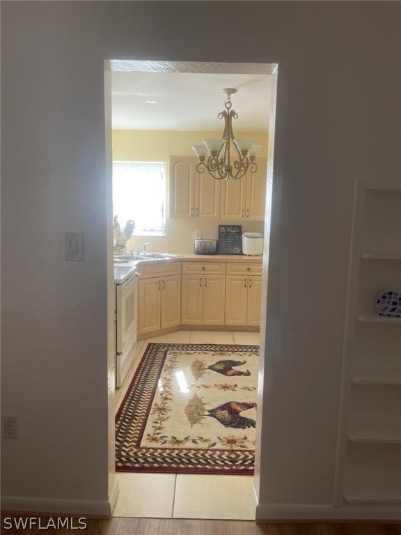 kitchen with light tile floors, sink, tasteful backsplash, stove, and an inviting chandelier