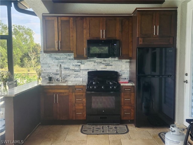 kitchen featuring black appliances, decorative backsplash, light stone counters, and sink