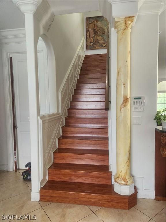 staircase featuring tile patterned flooring, crown molding, and decorative columns