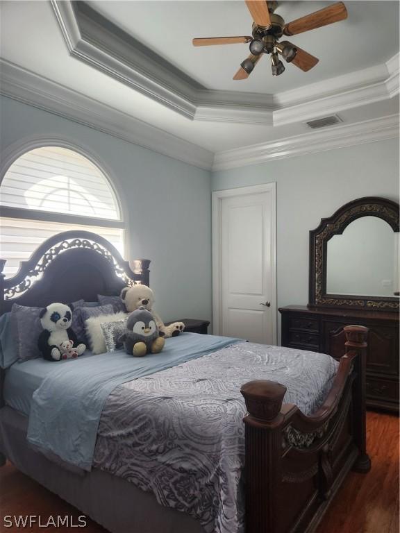 bedroom featuring ornamental molding, a raised ceiling, ceiling fan, and dark wood-type flooring