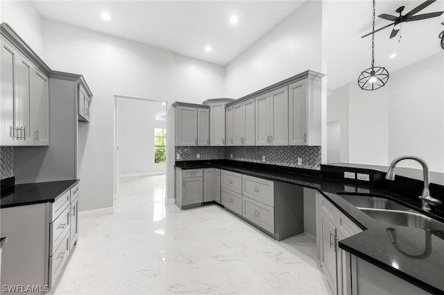 kitchen with gray cabinetry, a high ceiling, backsplash, sink, and ceiling fan