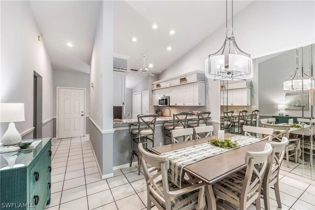 dining space featuring high vaulted ceiling, sink, light tile flooring, and ceiling fan with notable chandelier