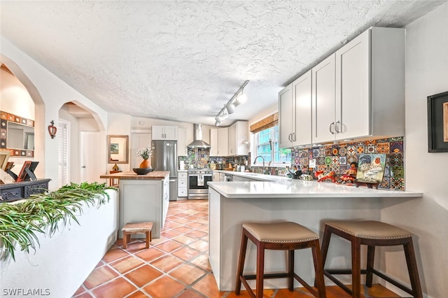 kitchen featuring light countertops, wall chimney exhaust hood, white cabinetry, and decorative backsplash