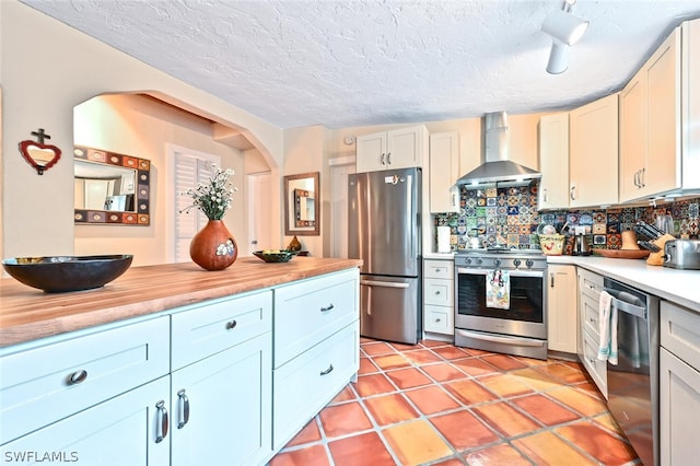 kitchen featuring stainless steel appliances, light countertops, decorative backsplash, white cabinetry, and wall chimney exhaust hood