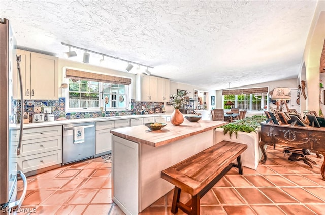 kitchen with a textured ceiling, stainless steel appliances, a breakfast bar, wood counters, and tasteful backsplash