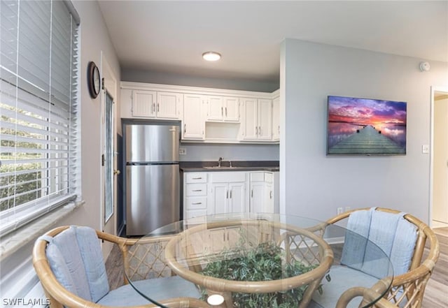 kitchen with white cabinets, hardwood / wood-style floors, stainless steel refrigerator, and sink