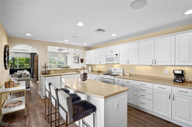 kitchen featuring a breakfast bar area, white cabinets, decorative light fixtures, and white appliances