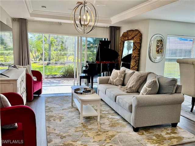 living room with light wood-type flooring, ornamental molding, a tray ceiling, a healthy amount of sunlight, and a notable chandelier