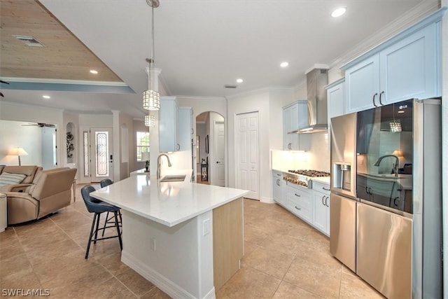 kitchen featuring wall chimney exhaust hood, sink, an island with sink, pendant lighting, and stainless steel appliances