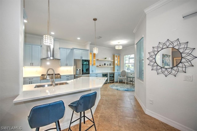 kitchen with decorative light fixtures, stainless steel fridge, a kitchen breakfast bar, kitchen peninsula, and wall chimney exhaust hood