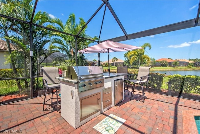 view of patio featuring an outdoor bar, a water view, glass enclosure, grilling area, and an outdoor kitchen