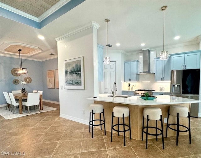 kitchen with a large island, sink, hanging light fixtures, and wall chimney range hood