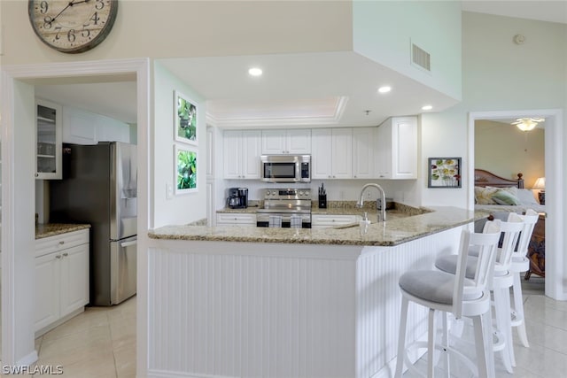 kitchen featuring appliances with stainless steel finishes, sink, white cabinets, light tile patterned floors, and kitchen peninsula