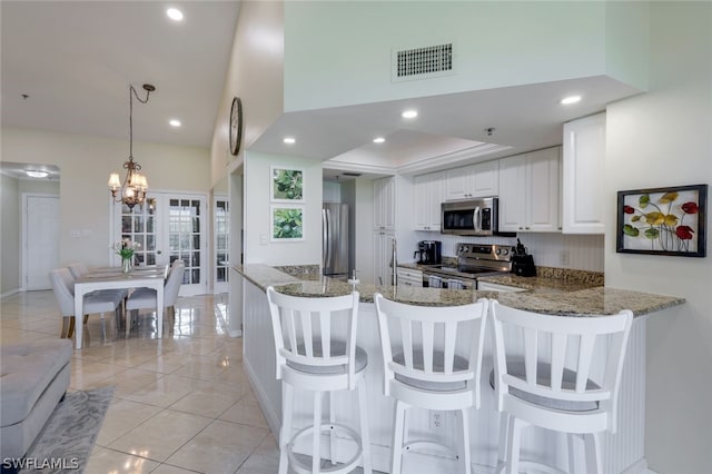 kitchen with appliances with stainless steel finishes, stone countertops, decorative light fixtures, white cabinetry, and kitchen peninsula