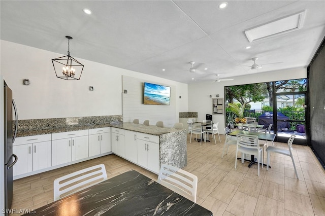 kitchen with stainless steel fridge, pendant lighting, dark stone countertops, and white cabinets