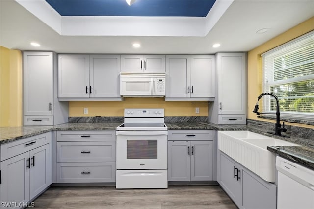 kitchen with white cabinets, white appliances, dark stone counters, and light wood-type flooring