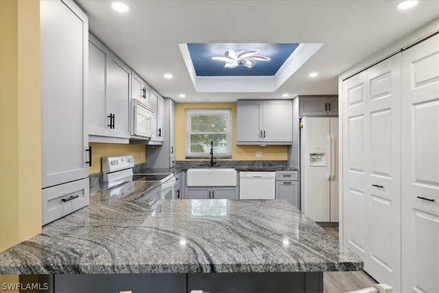 kitchen featuring sink, white appliances, a tray ceiling, kitchen peninsula, and light stone countertops