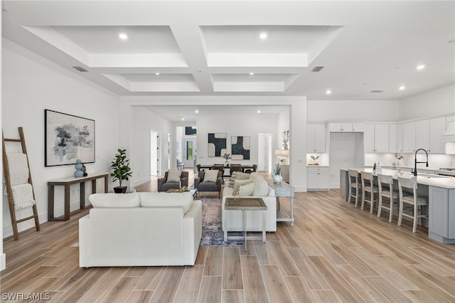 living room with beam ceiling, light hardwood / wood-style flooring, coffered ceiling, and sink