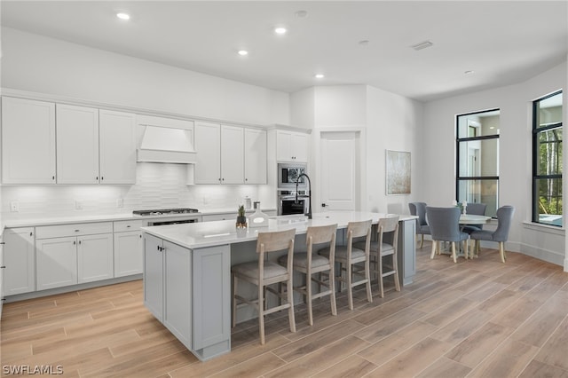 kitchen featuring white cabinets, custom range hood, stainless steel appliances, and a kitchen island with sink