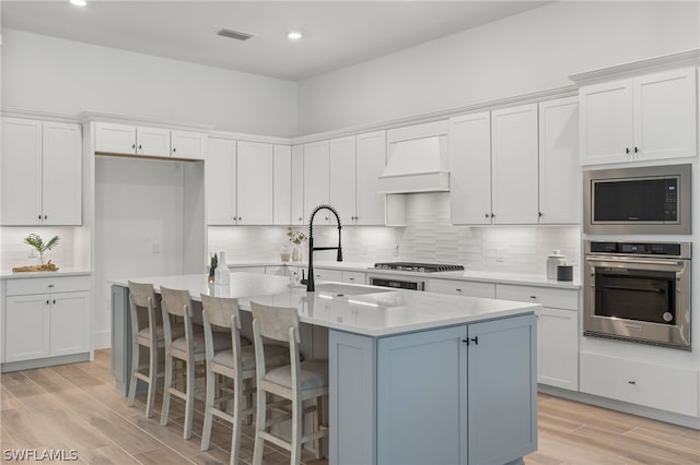 kitchen with white cabinetry, an island with sink, stainless steel appliances, and custom range hood