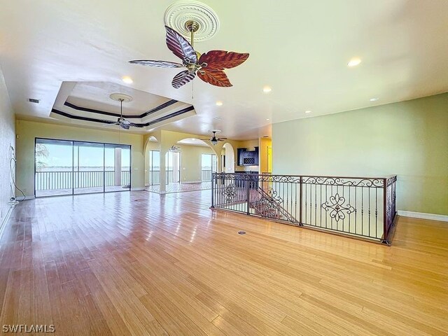 empty room featuring ceiling fan, a tray ceiling, light hardwood / wood-style flooring, and a wealth of natural light