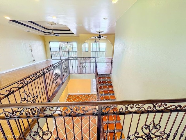 staircase featuring wood-type flooring, ceiling fan, and a tray ceiling